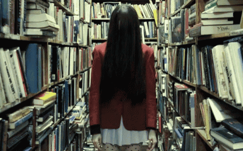 a woman in a red jacket is walking through a bookstore filled with books