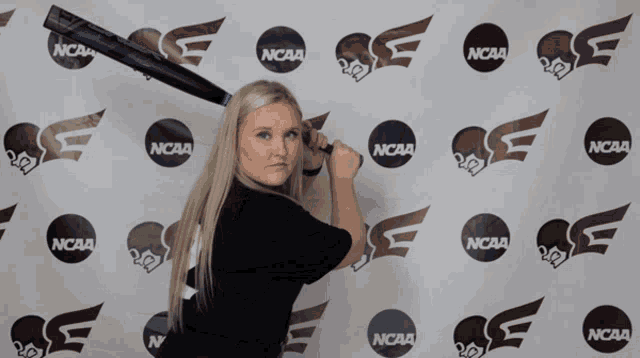 a woman holding a bat in front of a ncaa backdrop