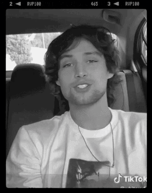 a black and white photo of a young man in a car with tiktok written on the bottom right