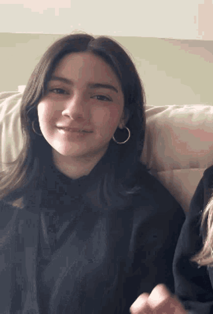 a girl wearing hoop earrings is sitting on a couch and smiling