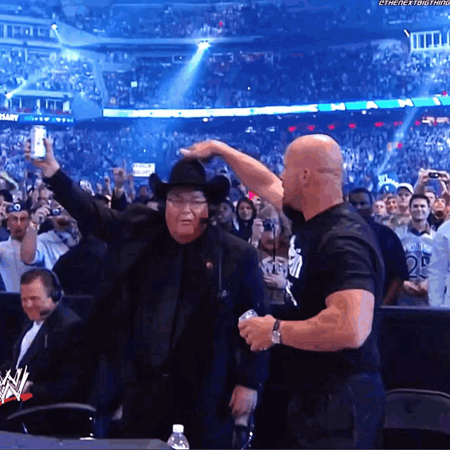 a man in a cowboy hat stands next to a man in a black shirt that says ' wwe ' on it