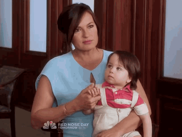 a woman is holding a baby in her arms with a nbc ad behind them