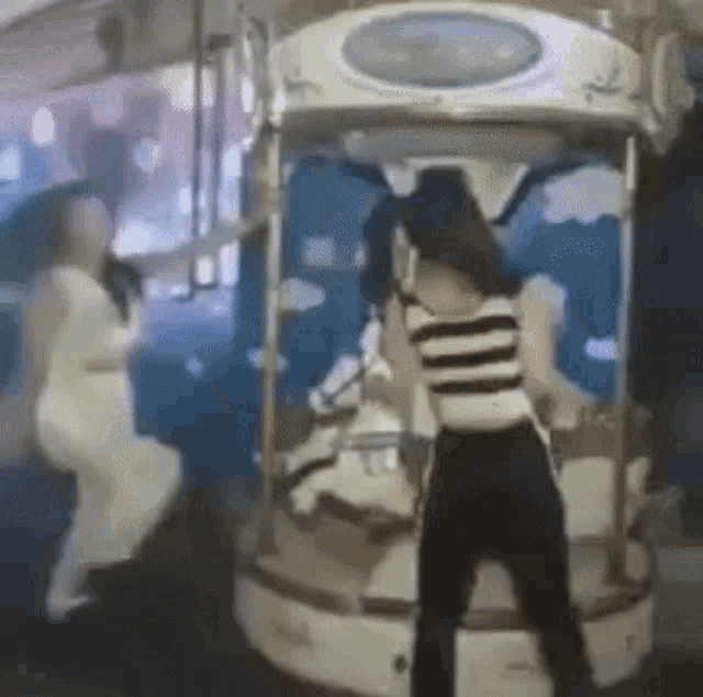two women are standing next to each other in front of a merry go round .