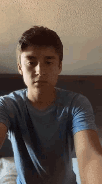 a young man in a blue shirt is standing in front of a bed