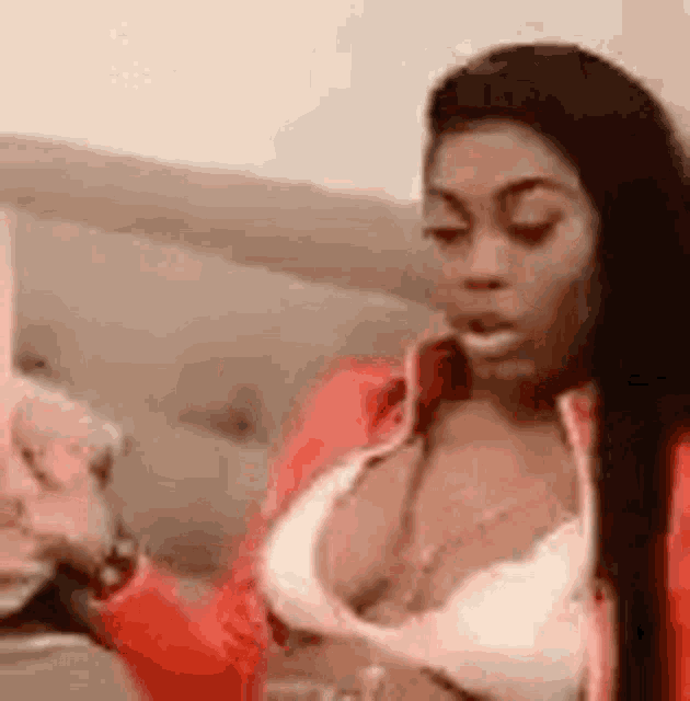 a woman in a bra and red jacket is sitting on a couch holding a glass of wine .