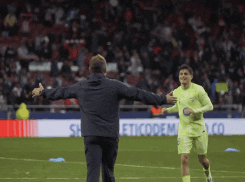 two soccer players are hugging each other on a field with a sign that says eticodem