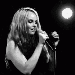 a black and white photo of a woman singing into a microphone .