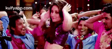 a group of people are dancing in a room with a woman in the middle .