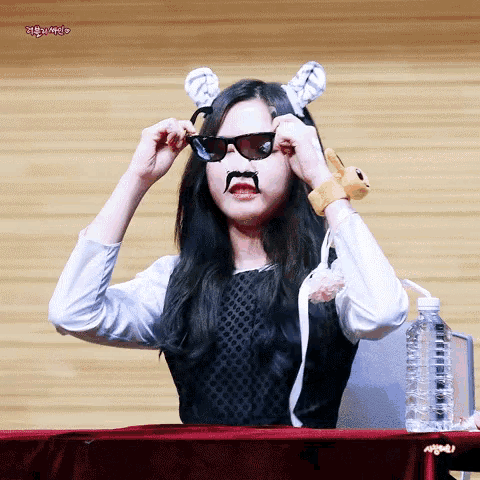 a woman wearing sunglasses and a fake mustache is sitting at a table