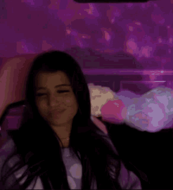 a woman is sitting in a dark room with a purple light behind her .