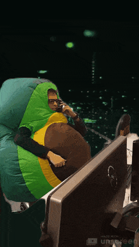a man in an inflatable kiwi costume sits in front of a dell computer monitor