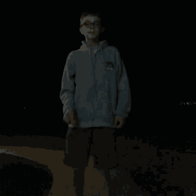 a young boy wearing glasses and a grey hoodie is standing in the dark