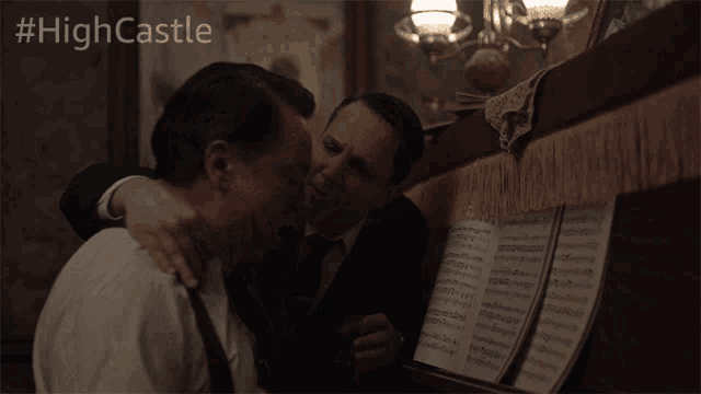 two men hugging in front of a piano with the hashtag #highcastle