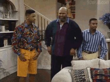 three men are standing in a living room in front of a couch and stairs .