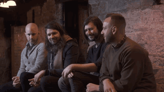 a group of men are sitting on a brick wall talking