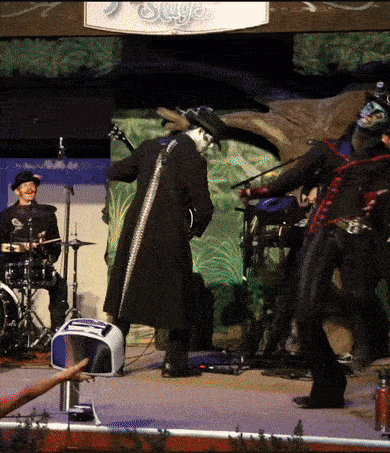 a man in a black coat is playing a guitar in front of a sign that says " skye "