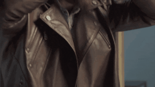 a man wearing a brown leather jacket holds his hand to his head