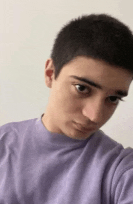 a young man in a purple sweater is taking a selfie with his phone .