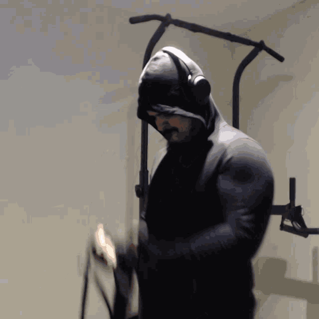 a man wearing headphones and a hooded sweatshirt stands in front of a pull up bar