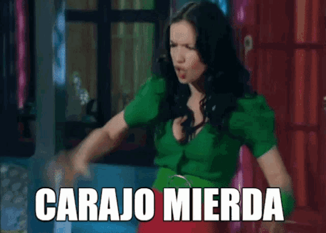 a woman in a green shirt is standing in front of a sign that says carajo mierda .