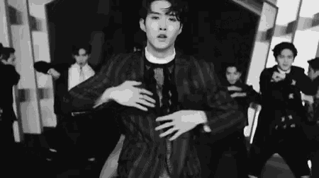 a black and white photo of a man in a suit dancing in front of a group of people .