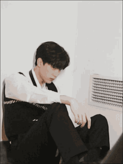 a man in a white shirt and black pants is sitting on the floor