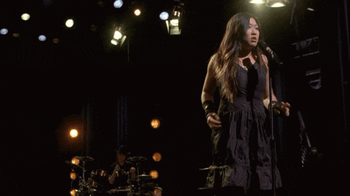 a woman in a black dress singing into a microphone
