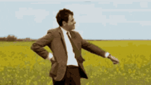 a man in a suit and tie is standing in a field with his arms outstretched .