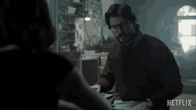 a man in a red sweater talks to a woman in a dark room with a netflix logo on the bottom