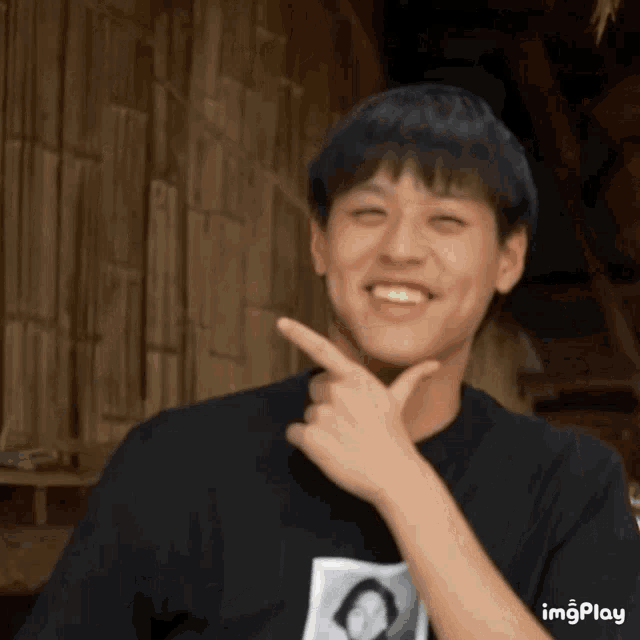 a young man in a black shirt is smiling and pointing his finger