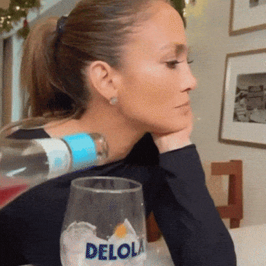 a woman is sitting at a table with a glass and a bottle of delola water on her back