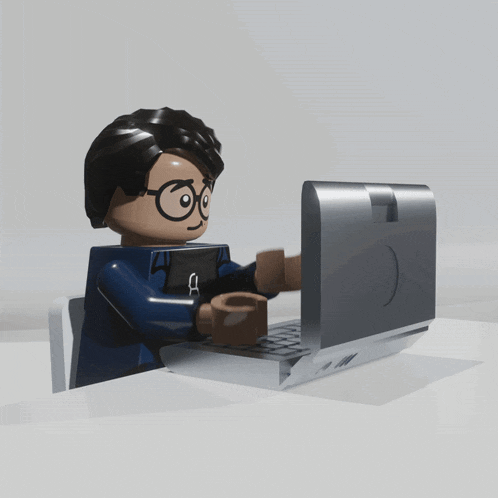 a lego figure is typing on a laptop with a smiley face on the screen