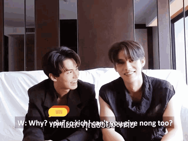 two young men are sitting on a couch and one of them is asking the other why