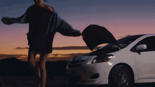 a woman stands next to a white car with the hood up
