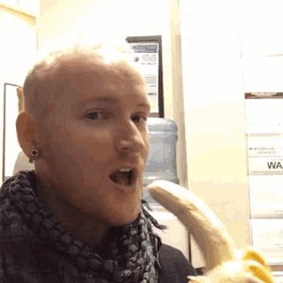 a man is holding a banana in front of a wall with a sign that says wa on it