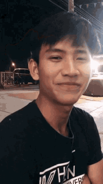 a young man wearing a black shirt with the word hn on it smiles at the camera .