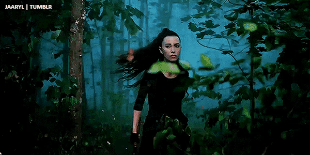 a woman with long black hair is standing in a dark forest with trees in the background