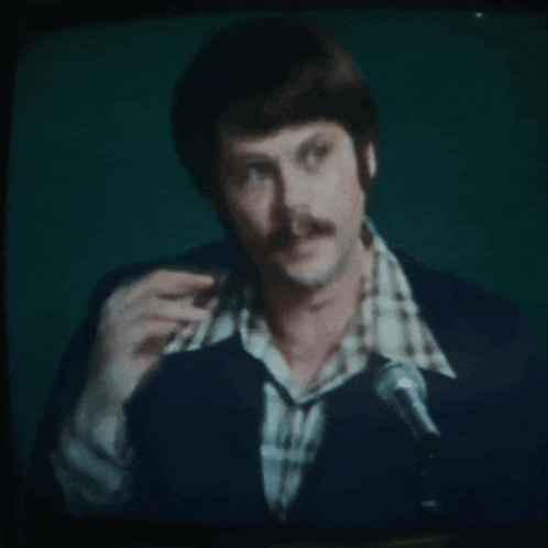 a man with a mustache is speaking into a microphone on a television screen