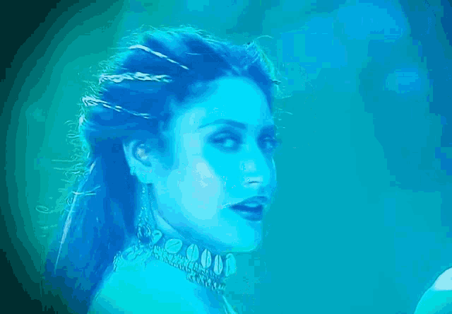 a woman with blue hair and a choker on her neck looks at the camera