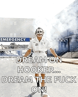 a man dressed as the joker is standing in front of an emergency room with smoke coming out of it .