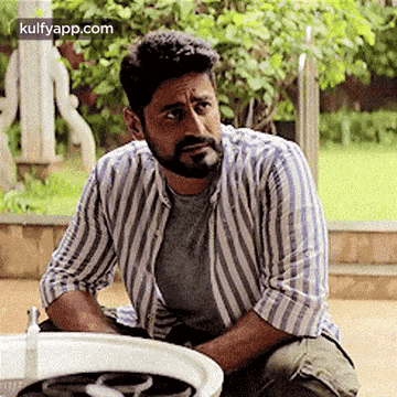 a man with a beard is sitting next to a washing machine and looking at it .