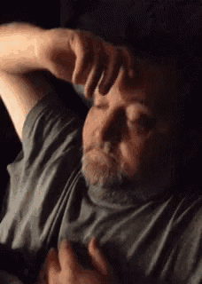 a man with a beard is laying on a bed scratching his forehead .
