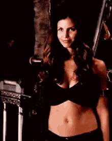a woman is standing in a dark room wearing a black bra and black pants .