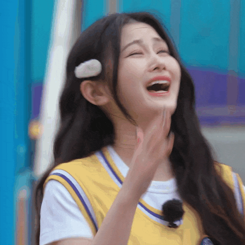 a woman wearing a yellow vest and white shirt is laughing with her mouth open