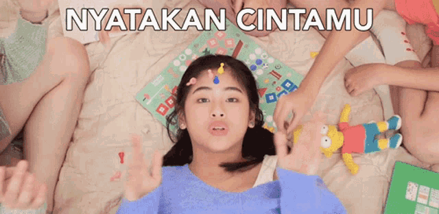 a girl laying on a bed with a board game and a stuffed bart simpson on her head