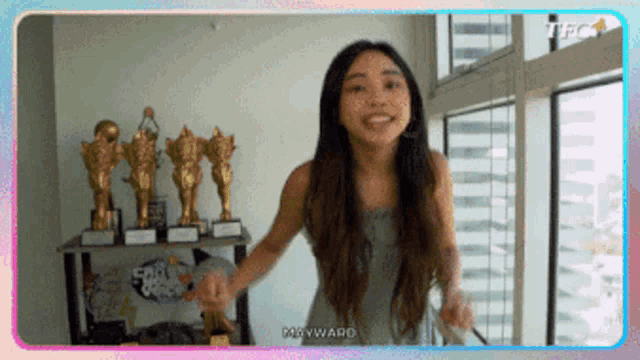 a woman is standing in front of a window with trophies on a table behind her .