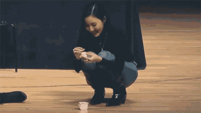 a woman is squatting down on the floor holding a small white cup