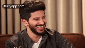 a man with a beard is laughing while sitting on a chair .