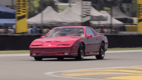 a red car is driving on a race track with a yellow sign that says ' motorsport ' on it