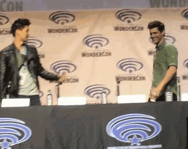 two men standing in front of a wall that says wondercon on it